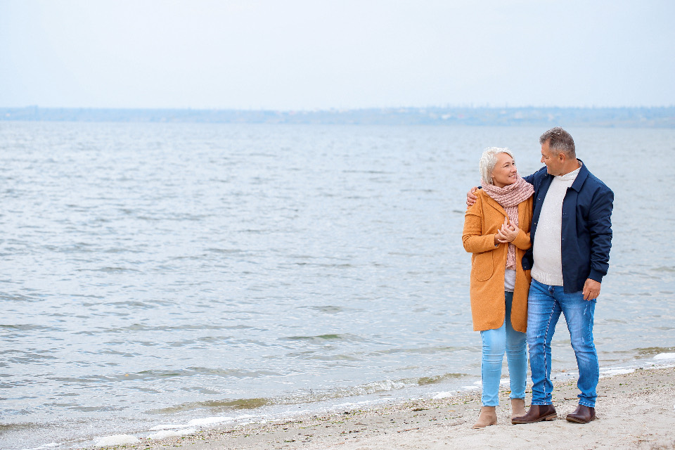 Ein älteres Paar geht Arm in Arm am Wasser entlang